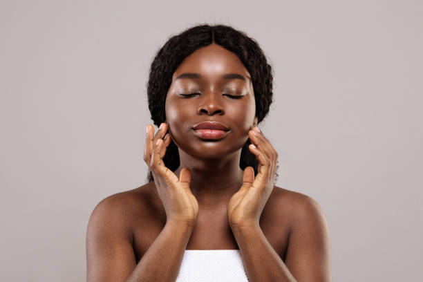 Dry Skin type- Closeup Shot Of Young Black Female With Closed Eyes Touching Her Face after a skincare routine and smiling.