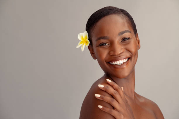 Smiling middle aged African woman with frangipani flower in hair looking at camera with a big laugh.