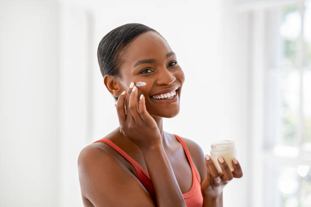 Smiling middle-aged skincare enthusiast woman applying hydrating moisturizer on her face, daily routine skin care. 