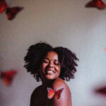 A black woman with her natural hair smiling with butterflies in the room
