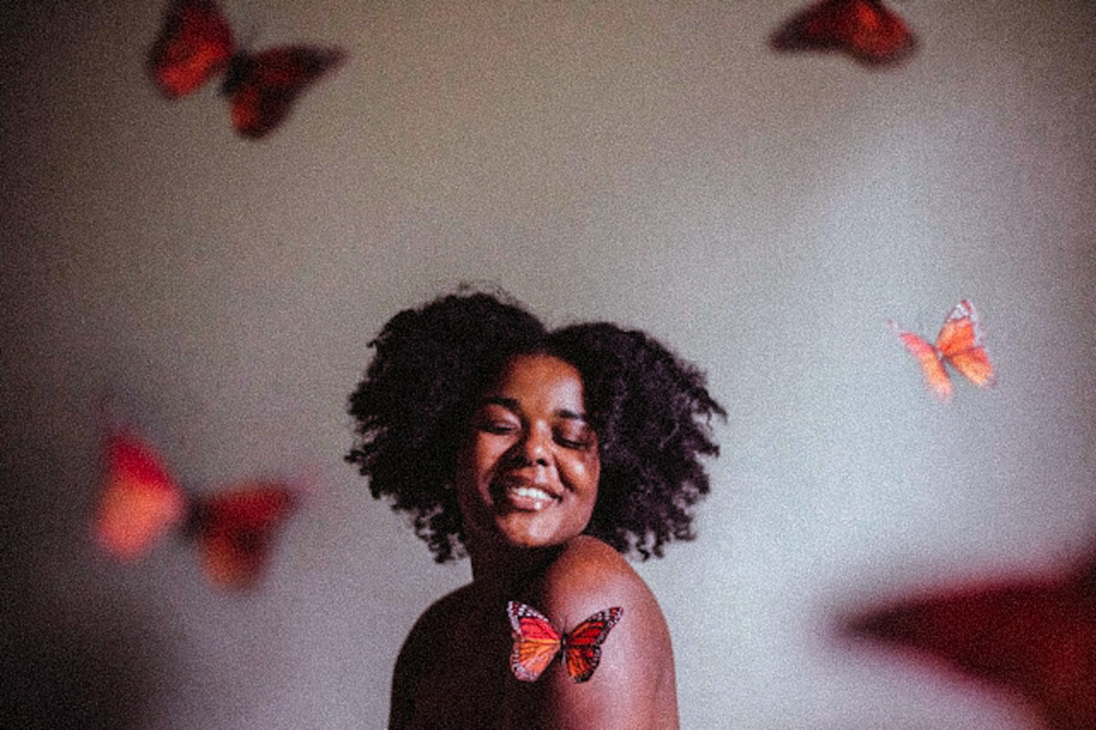 A black woman with her natural hair smiling with butterflies in the room